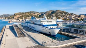 Un ferry moderne Corsica Ferries amarré au quai du port de Toulon sous un ciel méditerranéen lumineux, vue large sur l'infrastructure portuaire